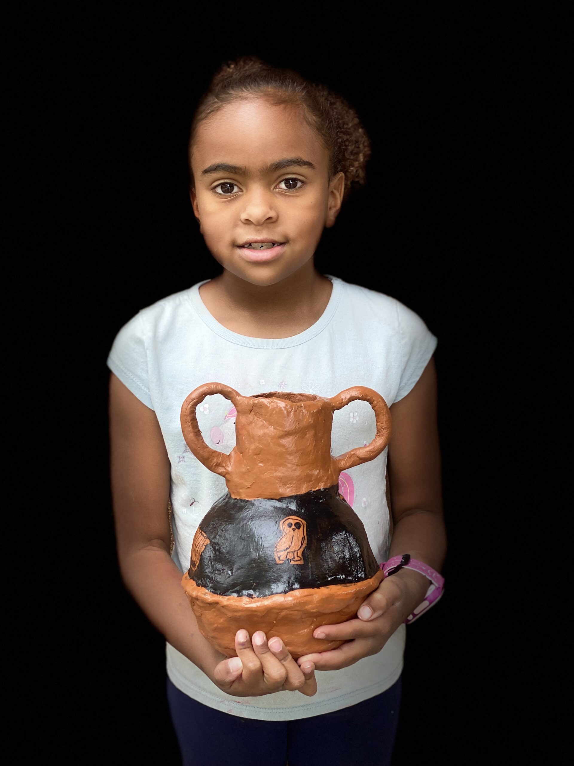 young girl proudly displaying her clay pot with an owl on it