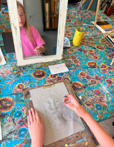 young student draws self portrait using mirror