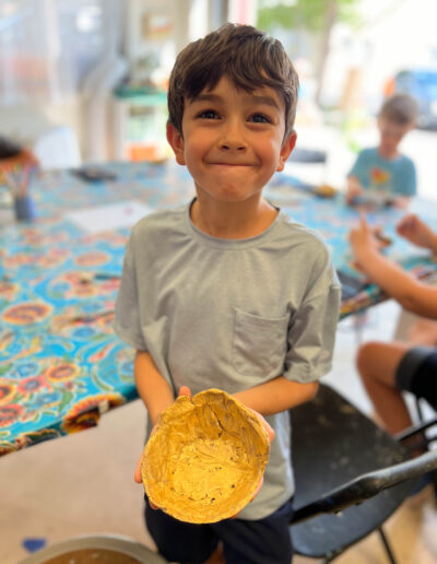 young boy has big smile while displaying his pottery artwork