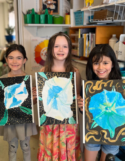 three young girls proudly display their artwork