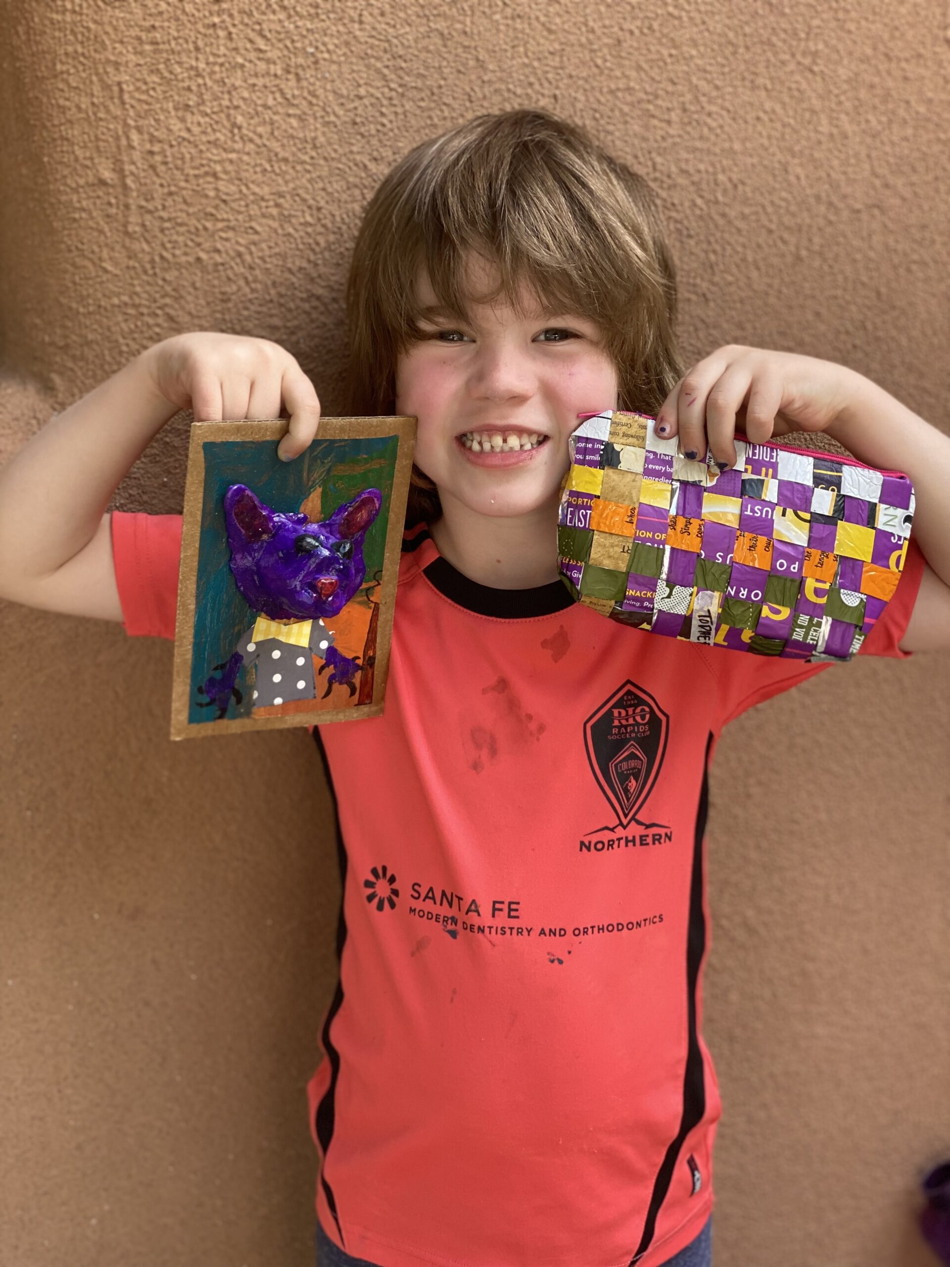 Young boy smiling and holding up two pieces of art he created