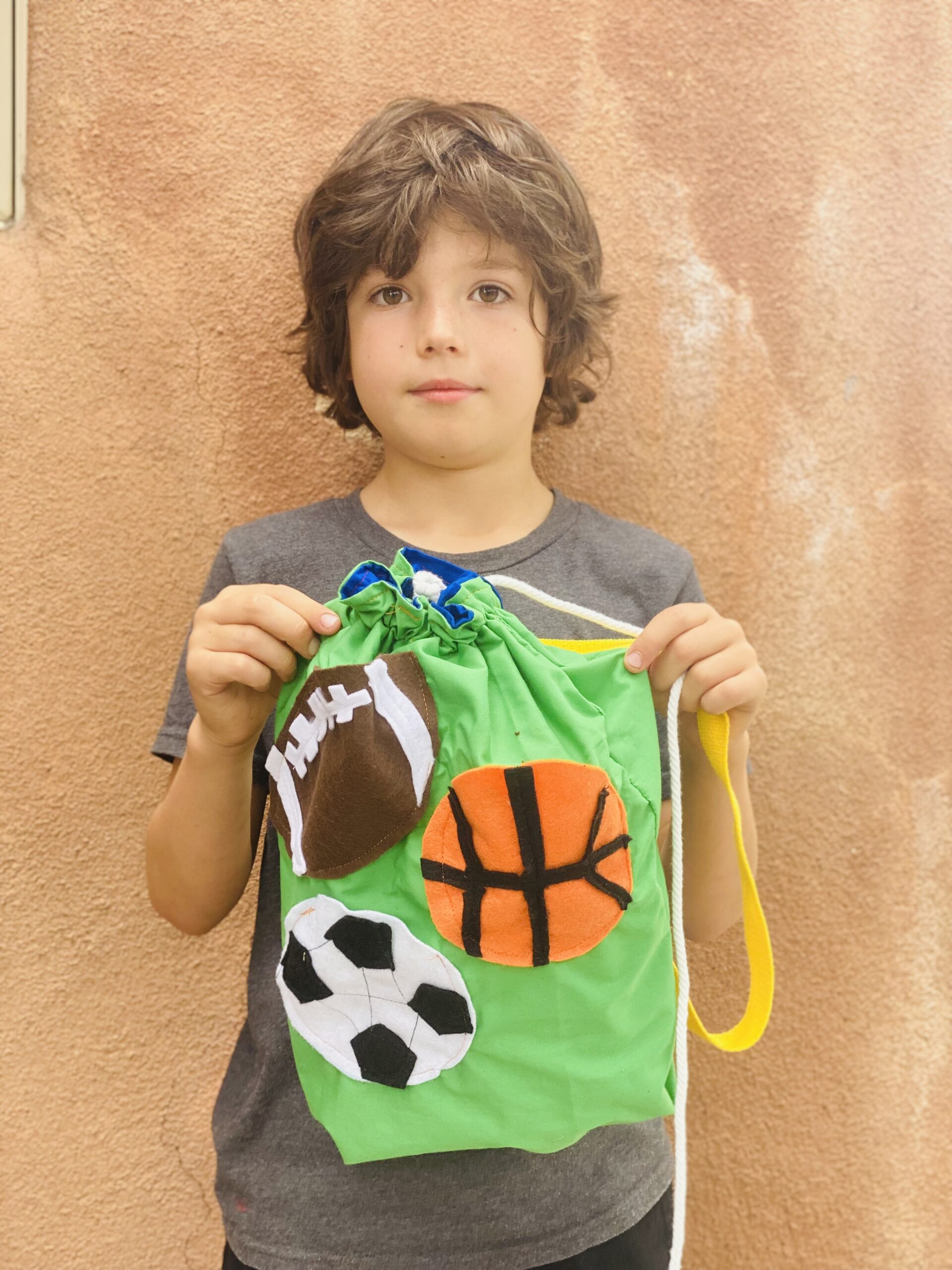 Young boy with brown hair holding cool bag with football basketball and soccer ball