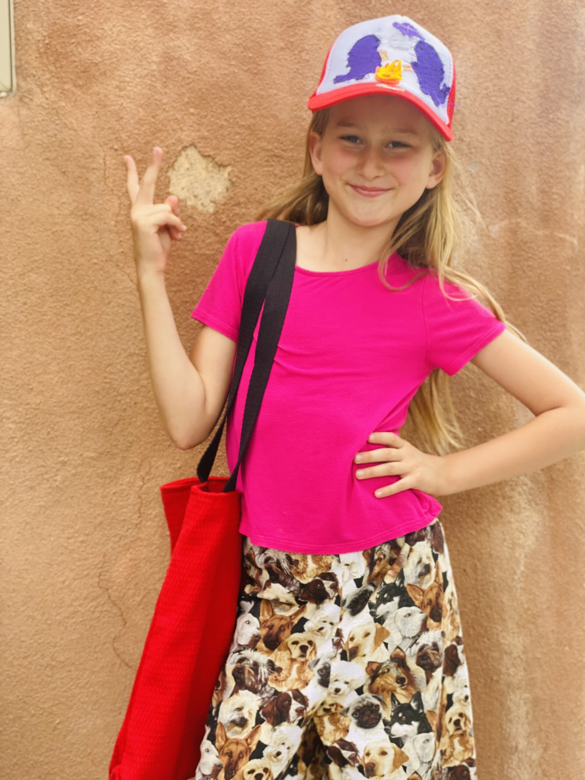 young girl in pink holding up peace sign with red bag