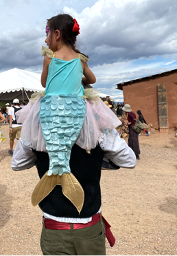 A four year old mermaid gets a ride on Dad's shoulders.