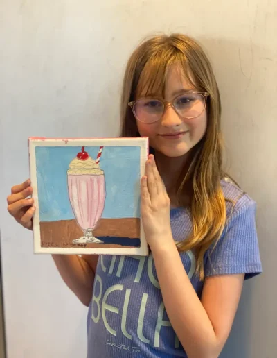 young student showing her painting of milkshake