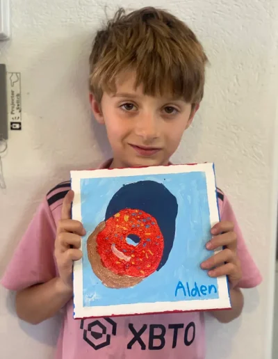 young student showing his painting of donuts